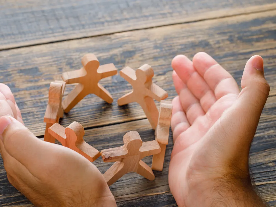 Two cupped hands around a circle of small wooden figures on a table